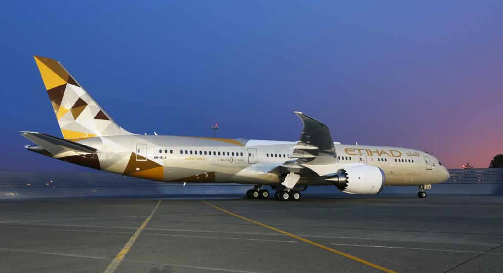 An Etihad Airways Boeing 787 on the apron at dusk, its tail carrying the Facets of Abu Dhabi livery.