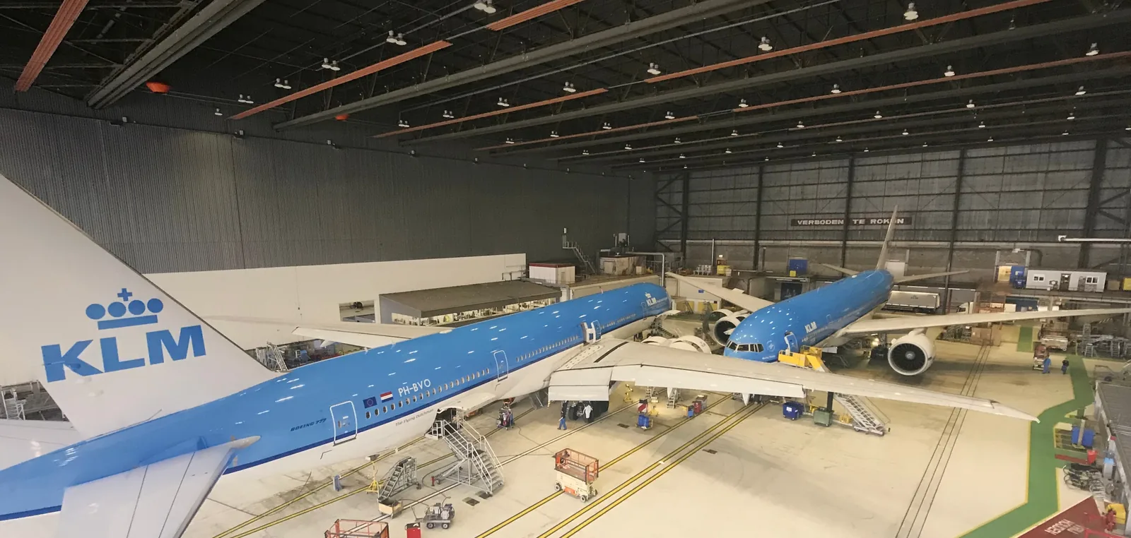 A wide view across the hangar floor, a KLM aircraft on its markings with work stands alongside.