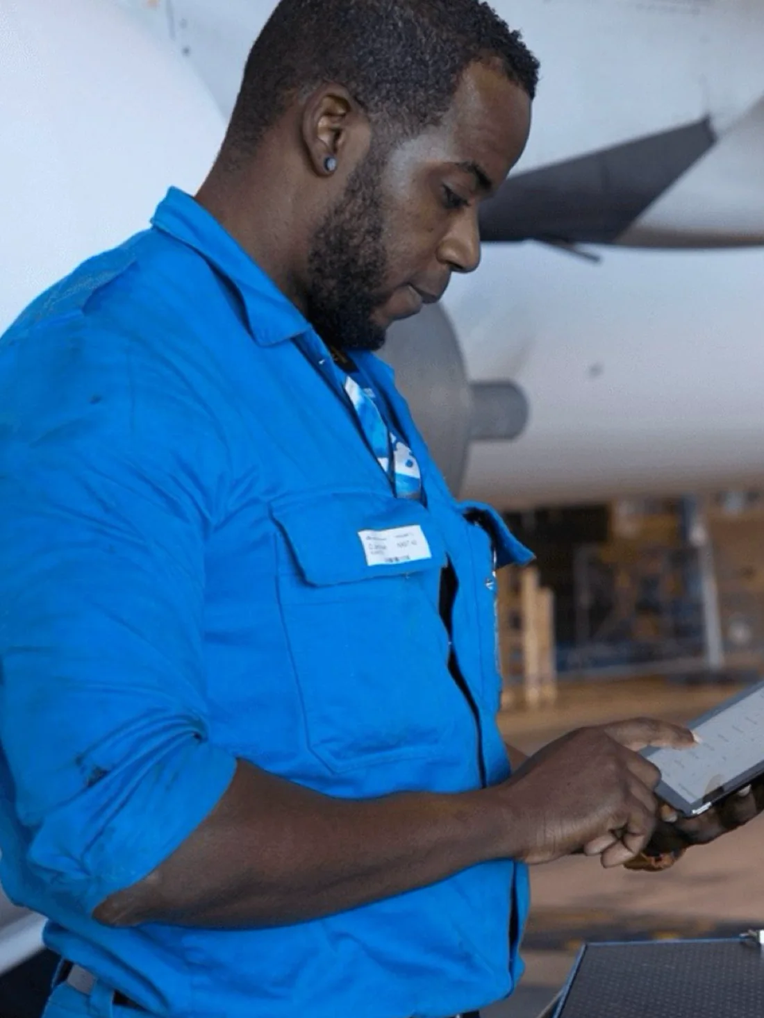 A KLM technician in blue overalls using the iMech iPad application beside an aircraft engine.