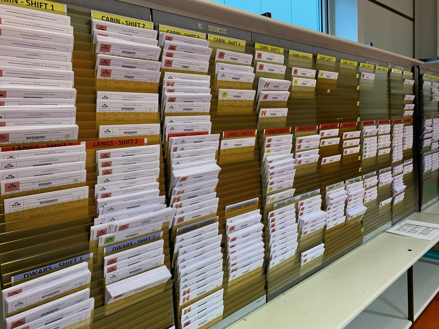 Wooden pigeonholes filled with printed task cards, labelled by area and shift.